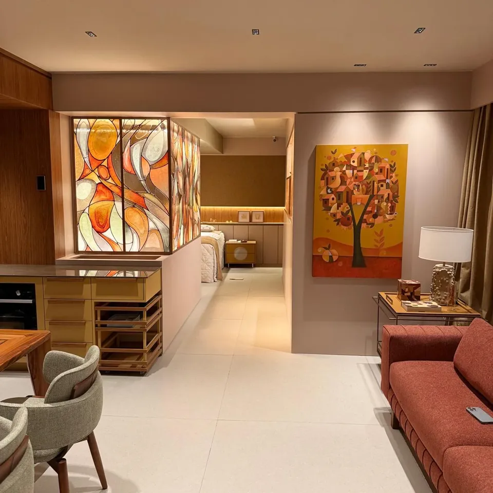 Ambiente da CASACOR com painel de madeira, divisória de vidro e sofá coral, integrado por marcenaria sob medida